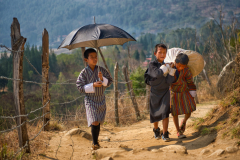 Drei Jungen mit Last und Sonnenschirm in Punakha